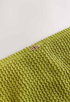 Tekstureeritud roheline kangas lainelise mustriga, millel on kuldse tooniga kinnituse detail. Materjal näib olevat kootud ja veidi veniv.