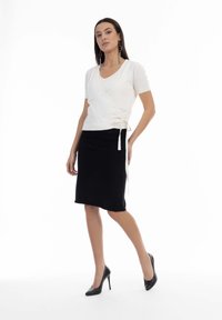 Hvid omslagstop med korte ærmer, parret med en sort knælang blyantskirt. Sorte højhælede sko fuldender outfittet.