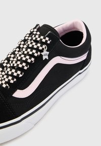 Black suede and canvas sneaker with pink accents, checkerboard laces, and a white rubber sole. Features a star-shaped Vans logo charm.