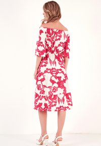 Off-the-shoulder dress in white with a red floral pattern. Features short, wide sleeves and a cinched waist, with a layered skirt.