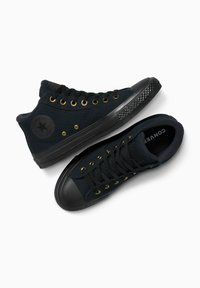 Zwarte canvas hoge sneakers met gouden veterogen, zwarte rubberen neuzen, gestructureerde zool en een cirkelvormig logo op de zijkant.