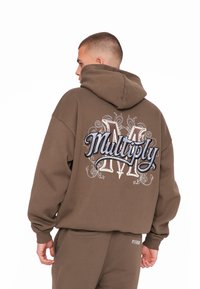 Brun hættepullover med et stort broderet logo "Multiply" på ryggen, fremhævet med detaljerede mønstre i lysere og mørkere tråde.