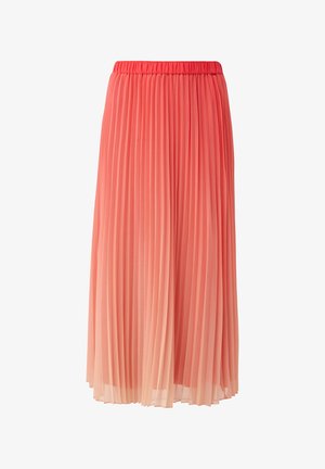 Femme portant un haut sans manches corail et une jupe midi plissée ombrée du rose au pêche, avec des sandales beiges, debout devant un fond blanc uni.