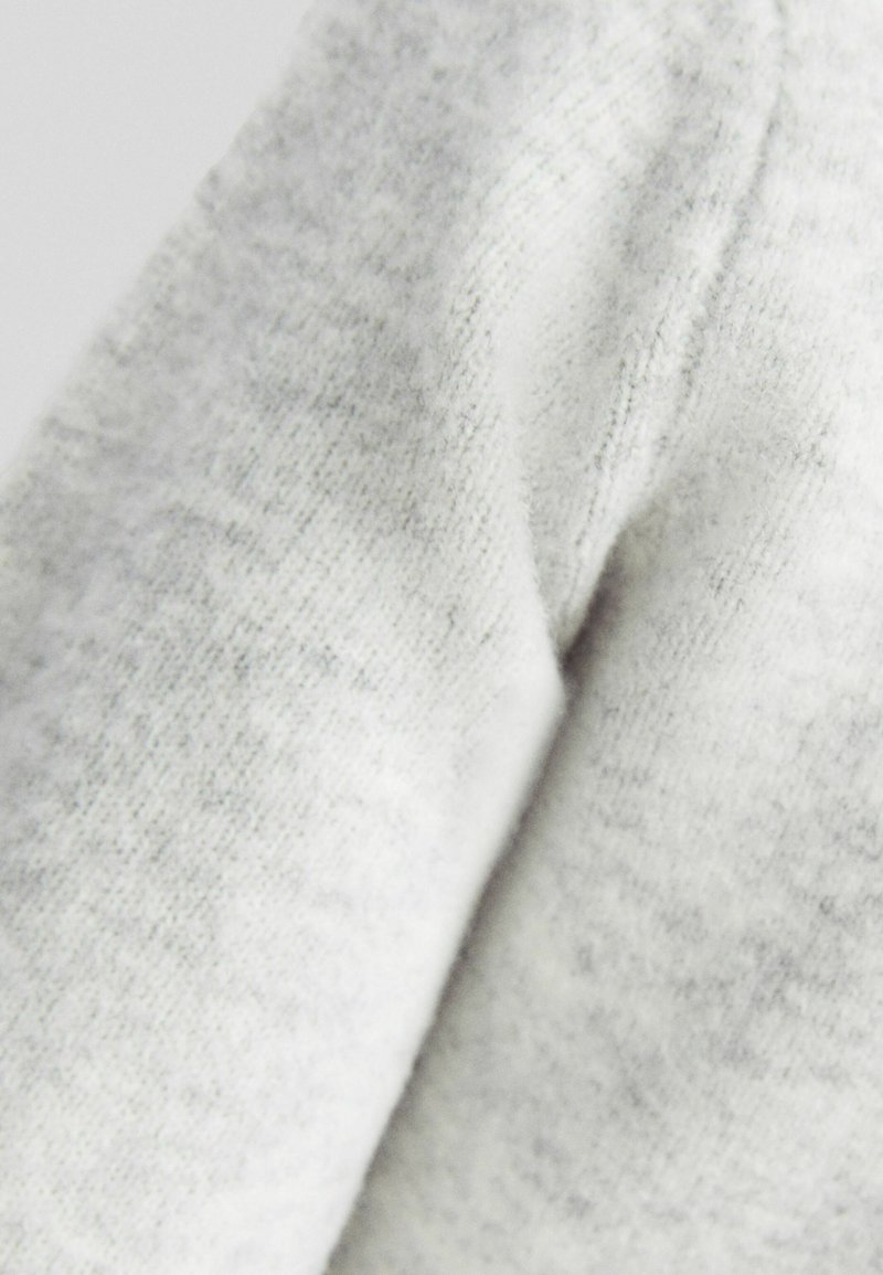 Hellgrauer Strickstoff mit weicher Textur, der subtile Variationen in der Schattierung und ein glattes Finish aufweist. Nahaufnahme des Gewebes.