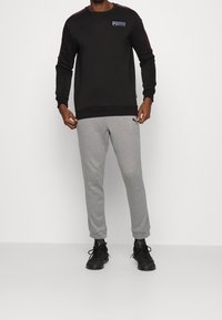 Černá mikina s logem PUMA, doplněná šedými tepláky. Součástí outfitu je volný střih a žebrované manžety a pas.