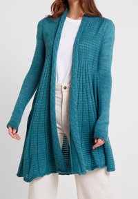 Lång teal-färgad kofta i strukturerad stickad kvalitet med öppen framdel, ribbade detaljer och intrikata mönster längs kanterna.