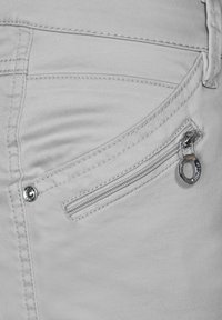Tela de mezclilla gris claro con un bolsillo lateral con cremallera. Presenta un tirador metálico redondo y un detalle de costura en contraste a lo largo de las costuras.