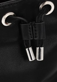 Sort læderpose med snoretræk, der har sølvhardware, tekstureret overflade og to metalspidser på snoretrækkene, hvilket fremhæver et strømlinet design.