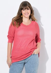 Suéter de punto coral con un patrón texturizado y cuello redondo acanalado, con mangas largas y un corte relajado, combinado con jeans claros.