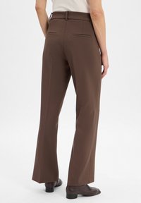 Braune maßgeschneiderte Hose mit geradem Bein, Gürtelschlaufen und zwei Gesäßtaschen. Das Material wirkt strukturiert und texturiert.
