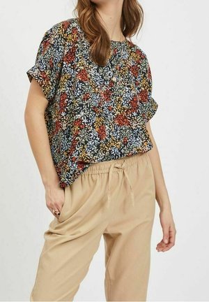 Top a maniche corte, dalla vestibilità rilassata, con un motivo floreale multicolore su sfondo scuro, abbinato a pantaloni beige con cintura regolabile in vita.