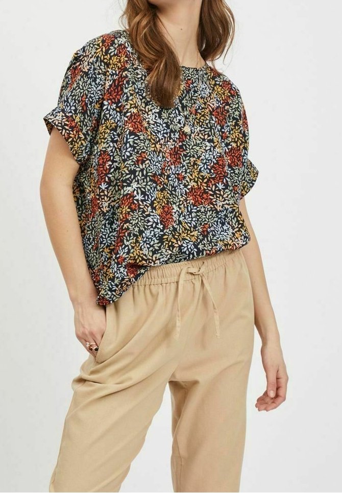 Lyhyet hihnat, rento paita, jossa on monivärinen kukkakuosi tummalla taustalla, yhdistettynä beigeihin, naruvedettävillä vyötäröhousuille.