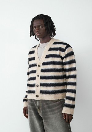 Gestreifter Cardigan in Beige und Schwarz, mit V-Ausschnitt, Knopfverschluss und gerippten Bündchen. Die Textur wirkt weich und fusselig.