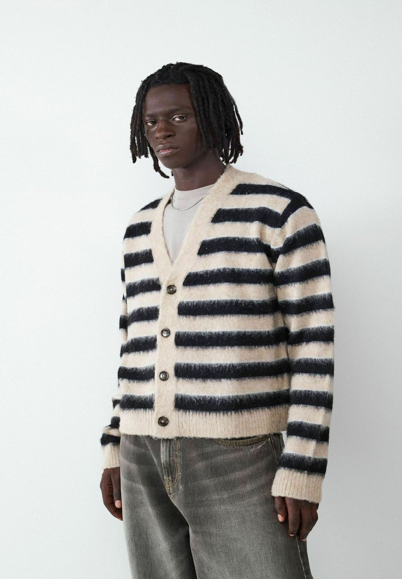 Pasiasty kardigan w beżowo-czarnym kolorze, z dekoltem w kształcie V, zapięciem na guziki i ściągaczami przy mankietach. Tekstura wydaje się miękka i puszysta.