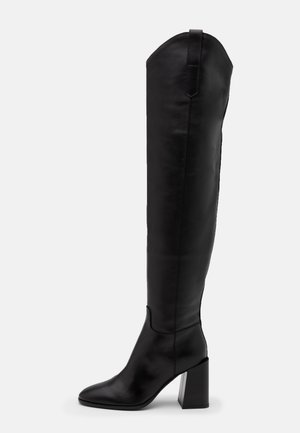 Czarne skórzane kozaki za kolano z ostrym noskiem, słupkowym obcasem oraz detalami szwów. Wyposażone w pętelkę z tyłu górnej części dla ułatwienia zakładania.