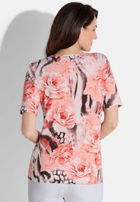 Bluse mit kurzen Ärmeln in floraler Optik, die ein pinkes und schwarzes Design mit Rosenmustern auf weichem Stoff zeigt, mit rundem Halsausschnitt und lockerer Passform.