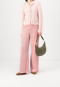 Rosa stickad kofta med guldfärgade knappar, kombinerad med rosa manchester byxor med vida ben. Håller en grön läderväska med kurvad design.