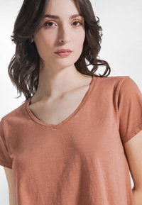 Roestkleurig, kort mouw V-hals T-shirt gemaakt van zacht, gestructureerd stof. Heeft een losse pasvorm met een ondiepe halslijn.