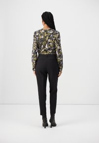 Blouse à manches longues à fleurs en noir, jaune et violet, associée à un pantalon noir ajusté. Bottines noires à talon léger.