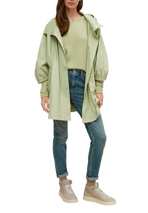 Hellgrüne, wasserdichte Jacke mit übergroßen gepufften Ärmeln, kombiniert mit einem hellgrünen Pullover, blauen Jeans und beigen High-Top-Sneakern.