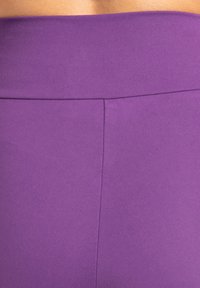 Paarse, aangesloten band ter hoogte van de taille van een naadloos kledingstuk, met een gladde textuur en voorzien van een verticale naaddetail aan de voorkant.