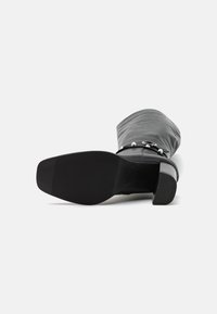 Botín de cuero negro hasta el tobillo con punta redonda, acabado suave y tacón bajo y cuadrado. Presenta un elegante detalle de hebilla en el lateral.