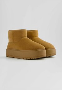 Brown suede ankle boots with a flat, textured sole, featuring a rounded toe and minimal stitching details.