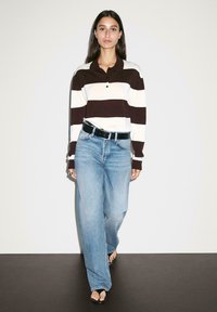 Brown and white striped long-sleeve polo shirt with a collar, paired with light blue wide-leg jeans and black belt, worn with black sandals.