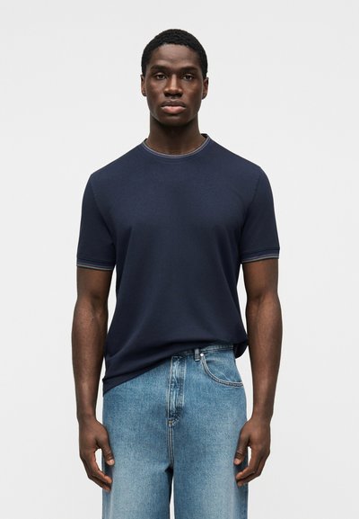 Μπλε σκούρο κοντομάνικο βαμβακερό μπλουζάκι με στρογγυλή λαιμόκοψη και πολύχρωμη διακόσμηση, με απαλή υφή, συνδυασμένο με ανοιχτόχρωμο μπλε τζην παντελόνι.