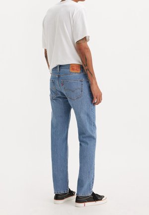 Jeans de mezclilla azul claro con un corte recto, presentan una etiqueta de cuero marrón en la parte trasera y detalles de costura sutiles. Combinados con una camiseta blanca.
