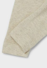 Tejido acanalado beige que muestra dos secciones superpuestas con un patrón texturizado natural y costuras visibles a lo largo de los bordes.