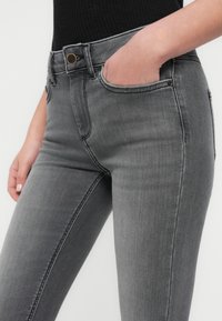 Γκρι τζιν παντελόνι από τζην ύφασμα με μέση μεσαίου ύψους, εφαρμοστή γραμμή και σχεδιασμό με πέντε τσέπες. Διαθέτει διακριτικές ραφές και κλείσιμο με μεταλλικό κουμπί.