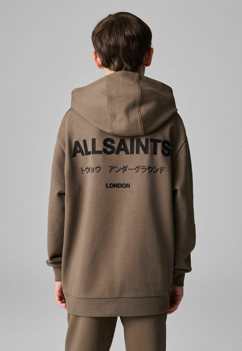 Tamnica s kapuljačom u smešanoj smešavini pamuka u smeđoj boji, s velikim crnim tekstom na leđima, s natpisima "ALLSAINTS" i "LONDON." Labav kroj i rebraste manžetne.
