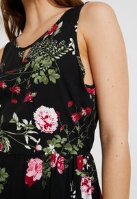 Blommig klänning med svart bakgrund, blommönster i rött och vitt, ärmlös design med nyckelhålsringning och en svävande silhuett.