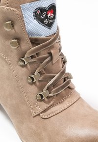 Bottine beige en daim avec lacets en velours, œillets métalliques et un patch bleu sur la languette présentant un cœur, un cheval et le texte « Je t'aime ».