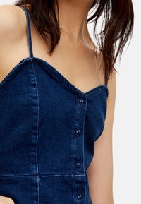 Denim dress in dark blue with thin straps, a sweetheart neckline, and front button closure. Features a fitted bodice and structured seams.