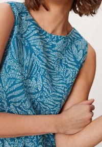 Robe sans manches bleue avec un motif texturé de lignes et formes blanches, dotée d'un col rond et d'un tissu doux.