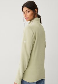 Giacca in fleece verde chiaro con colletto alto, maniche lunghe e logo ricamato sulla manica sinistra. Tessuto morbido e design aderente.