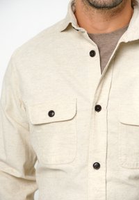 Beige button-down shirt van textiel met een structuur, met twee borstzakken met zwarte knopen en een button-down kraag.