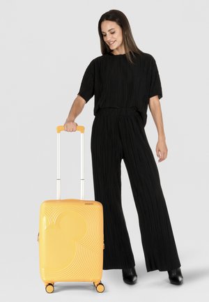 Valise rigide jaune avec une texture circulaire et un motif Mickey Mouse, poignée rétractable, 4 roues et ferrures accentuées.