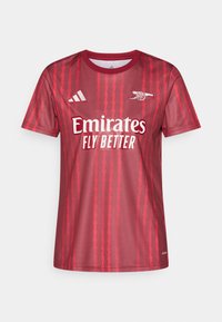 Κόκκινη αθλητική φανέλα με κοντά μανίκια που διαθέτει ζιγκ-ζαγκ σχέδια, λευκό λογότυπο "Emirates Fly Better" και λογότυπο Adidas στο στήθος. Ομαλή υφή υφάσματος.