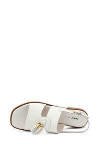 Sandal in pelle bianca con due cinturini larghi, tacco basso e una frange decorativa in argento e oro. Texture liscia con suola piatta.