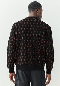 Felpa nera con stampa integrale di motivi decorativi arancioni. Collo e polsini a coste, vestibilità rilassata e tessuto liscio.