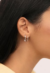 Pendiente de aro de plata con un pequeño charm en forma de estrella colgante. La vista en primer plano muestra un acabado pulido y un diseño sencillo, que realza la oreja.