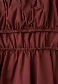 Tissu rouge foncé avec des bandes élastiques froncées créant des sections froncées horizontales.