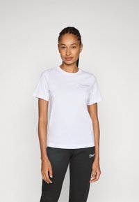 Witte katoenen t-shirt met korte mouwen, ronde halslijn en geborduurd logo in lichtgrijs. Gecombineerd met zwarte broek met een vergelijkbaar logo.
