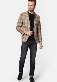 Beżowo-brązowy marynarka w kratę z wyciętymi klapami, zestawiona z czarnym t-shirtem i ciemnymi, dopasowanymi dżinsami. Uzupełniona czarnymi sneakersami.