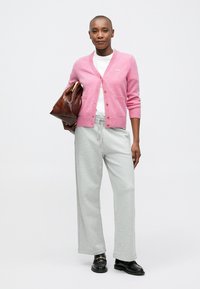 Rosa cardigan med ribbade ärmar och en liten broderad detalj, i kombination med grå vida sweatpants och svarta loafers, hållande en brun väska.