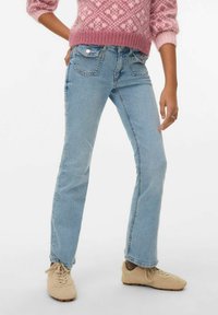 Svijetloplave traperice ravnog kroja, s pet džepova i vidljivim šavovima, uparene s bež tenisicama od brušene kože.