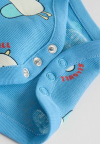 Vêtement bébé bleu côtelé avec boutons-pression et imprimés d'animaux de dessin animé, comprenant une partie d'un oiseau et un texte rouge.